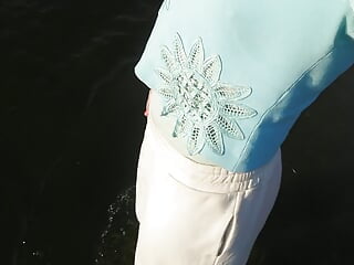 Trans girl swimming in the lake in clothes blue blouse and white-milk pants.
